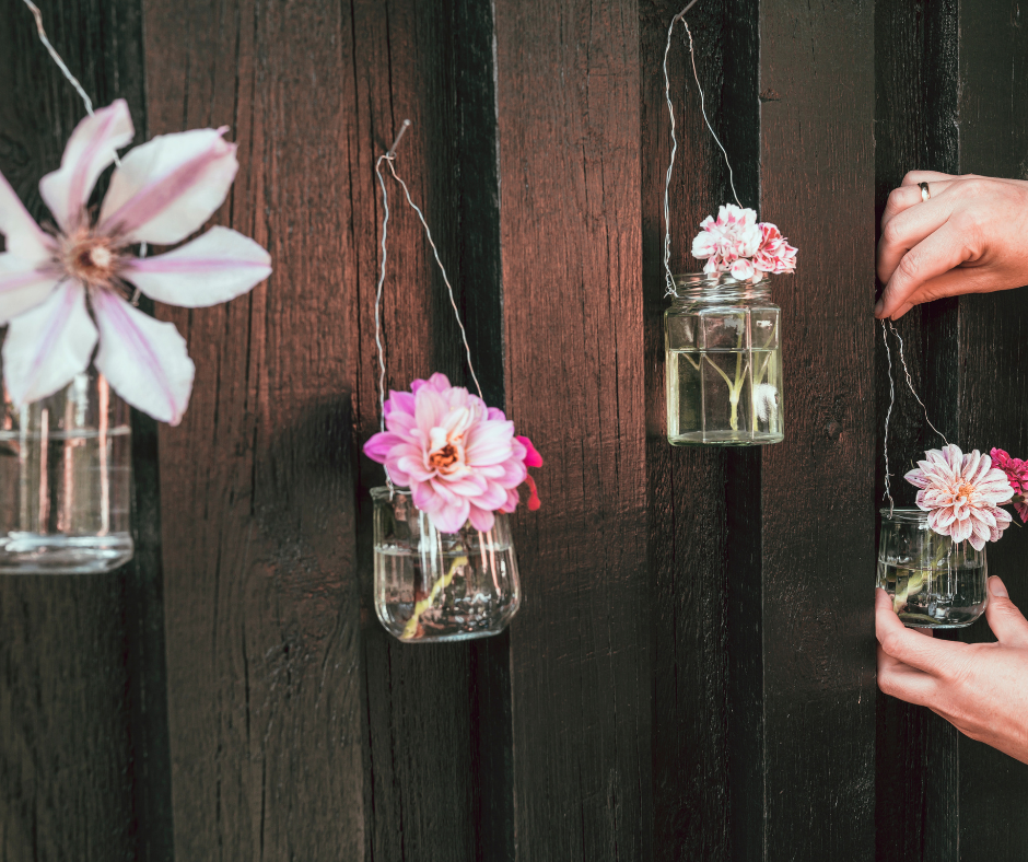 Glass jars upcycled into vases for 4 pink flowers hung on a brown wall