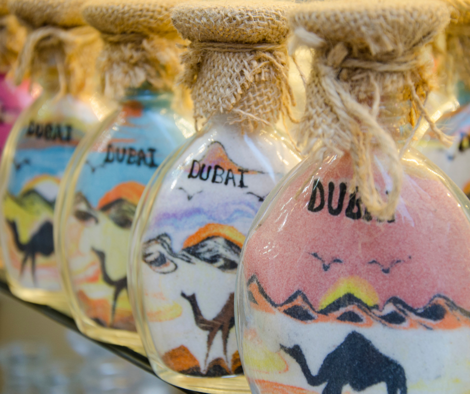 4 glass bottles with sand art with a drawing of a camel and the word Dubai