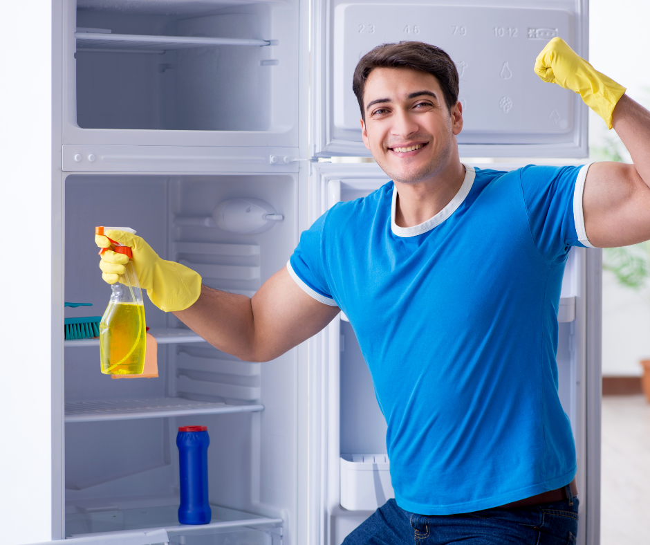 Man in a blue t-shirt with yellow gloves and a spray bottle cleaning a fridge