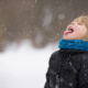 Photo of young child dressed in winter clothing catching snowflakes on his tongue