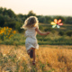 Young girl running away from us holding a windmill in a summery field of sunflowers