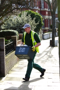 A household waste collector on a street holding a recycling box