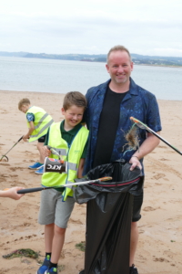 A dad and his son smile for the camera while litter picking at Exmouth beach.