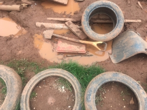 Assorted items like a spade, plastic chair seat, planks and tyres lying in muddy piles for loose parts play at Whipton Barton Junior School