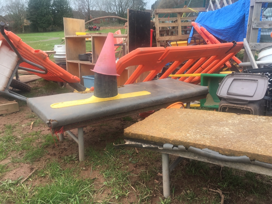 mixed pile of loose parts play equipment at Whipton Barton Junior School including bollards, plastic fences, shelves, tarps, pallets.