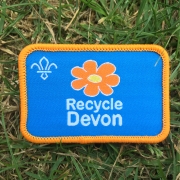 Close up of a Recycle Devon Scout Badge lying on grass