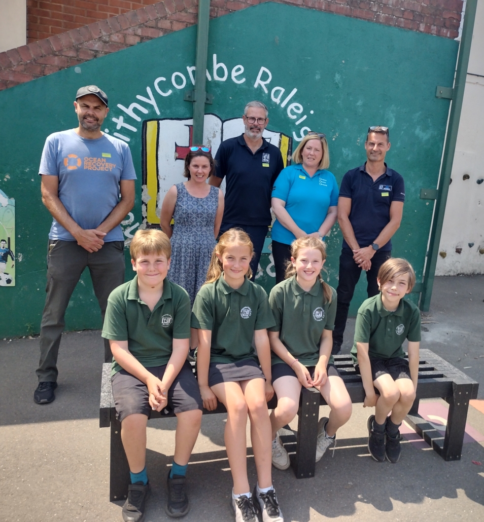 Children at Withycombe Raleigh Primary school sat on a bench, with representatives from their school, Resource Futures, Devon Contract Waste and the Ocean Recovery Project stood in a row behind them