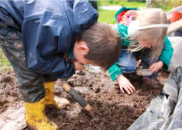 Image of two children with magnifying glasses looking in the mud for minibeasts
