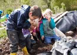 Children using magnifying glasses to study compost in an outdoor environment