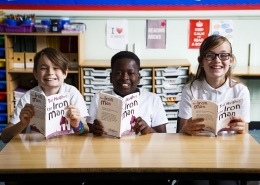 3 smiling children reading the book The Iron Man by Ted Hughes