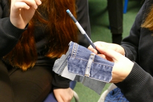 Young people holding a pencil made from denim and a piece of denim material