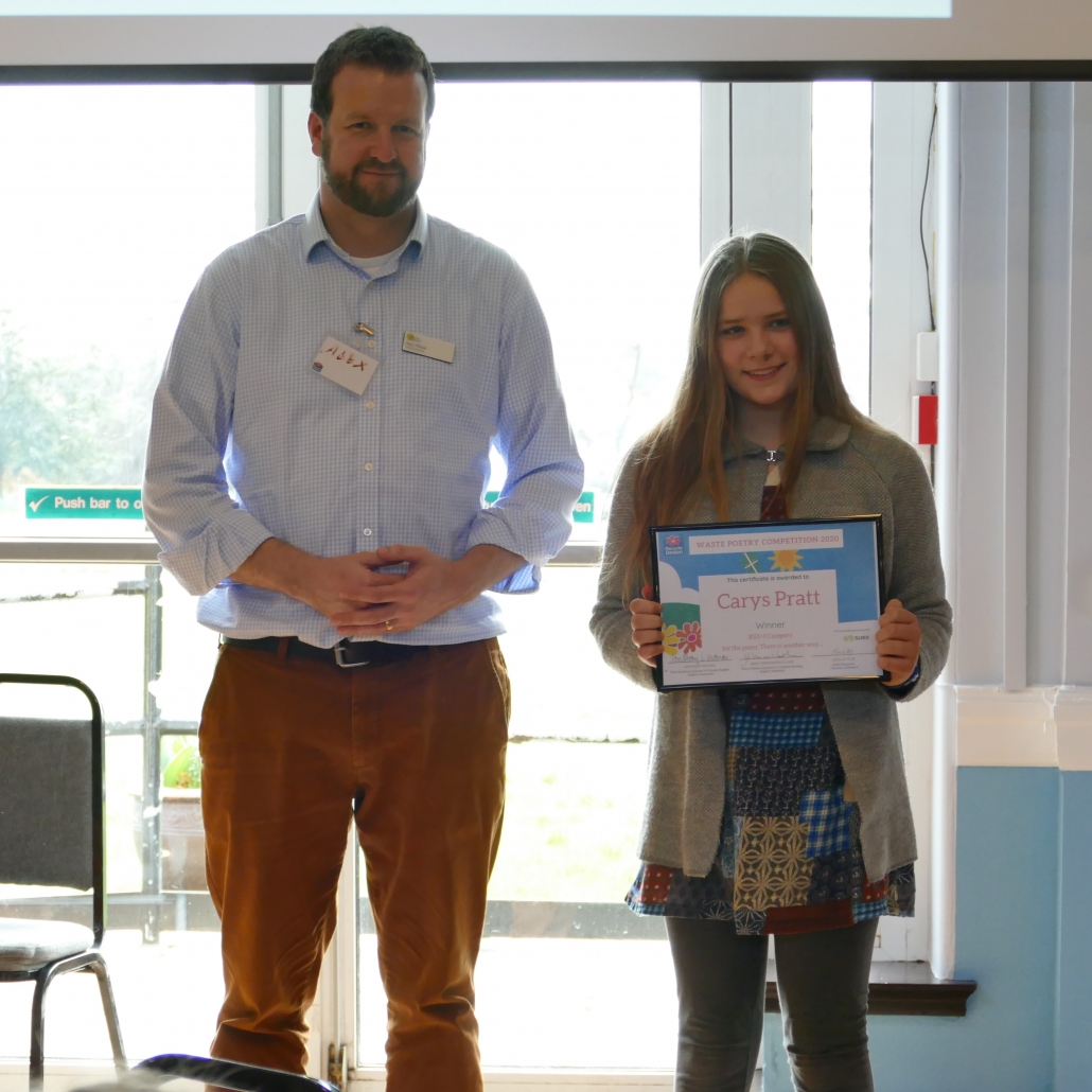 Alex Kittow stands alongside Carys Pratt who is holding her award for her winning poem. They are both smiling at the camera.