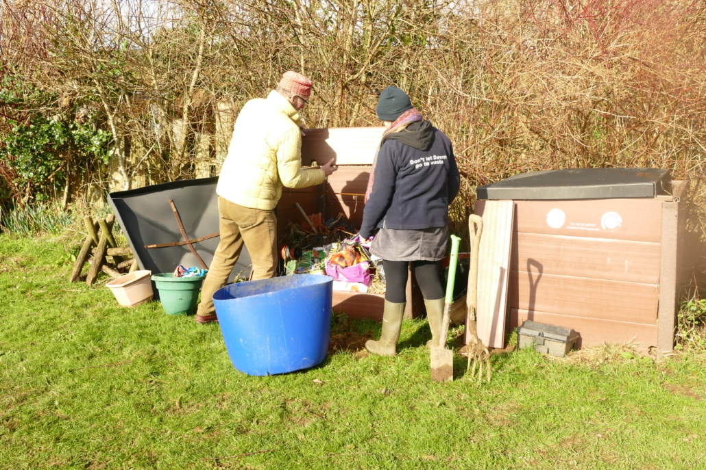 Two adults look inside a compost bin