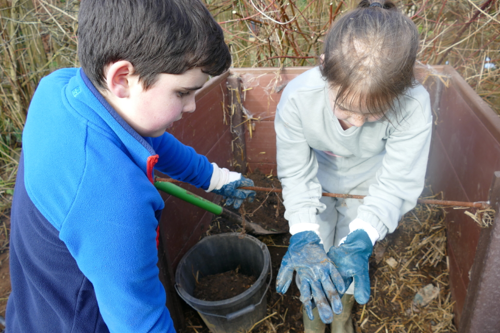 Two childre wearing gloves, one shows the other a bug found in compost