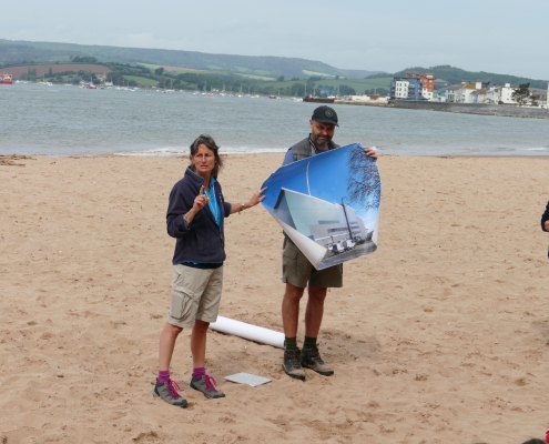 Two adults holding image of the energy from waste building in Exeter on a beach