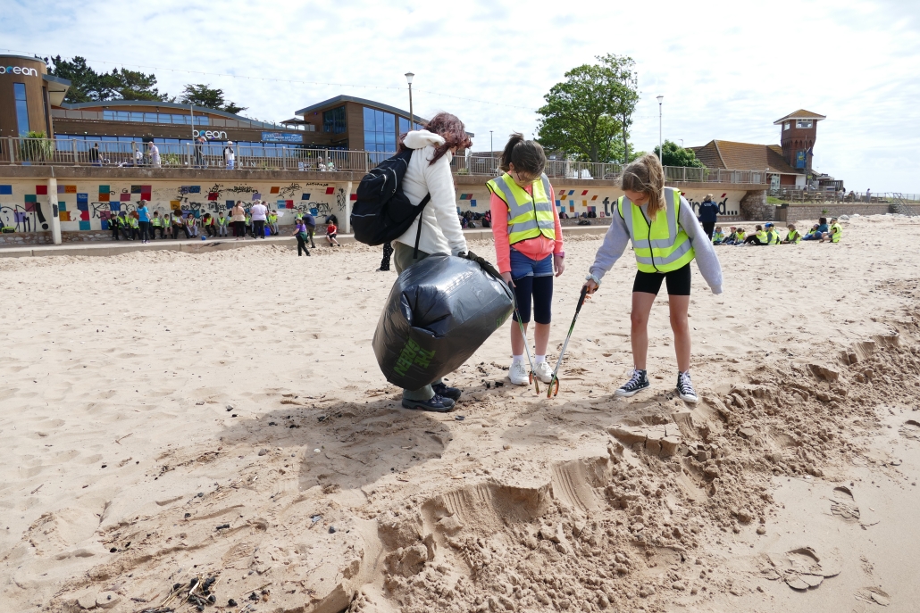Woman and two children using litter pickers and a black bin bag to collect rubbish on a beach
