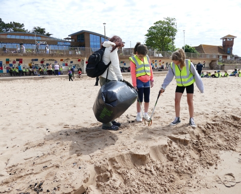 Woman and two children using litter pickers and a black bin bag to collect rubbish on a beach