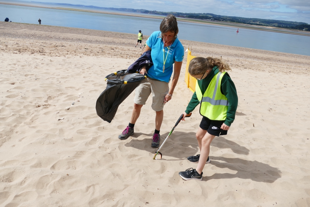 Adult and child collecting litter on a beach with bin bag and litter picker