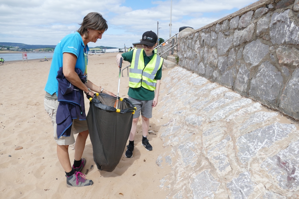 Adult and male children collecting litter on a beach with litter picker and bin bag