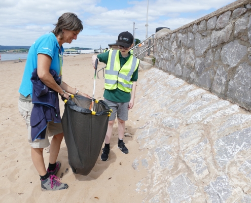 Adult and male children collecting litter on a beach with litter picker and bin bag