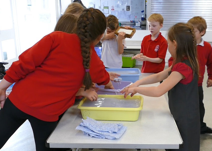 Children using trays of newspaper and water to make new paper