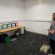 Two visitors from ROC creative holding beanbags, looking at five coloured buckets placed on a table.