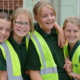 Four young girls in high-vis vests smiling at the camera, while hugging each other.