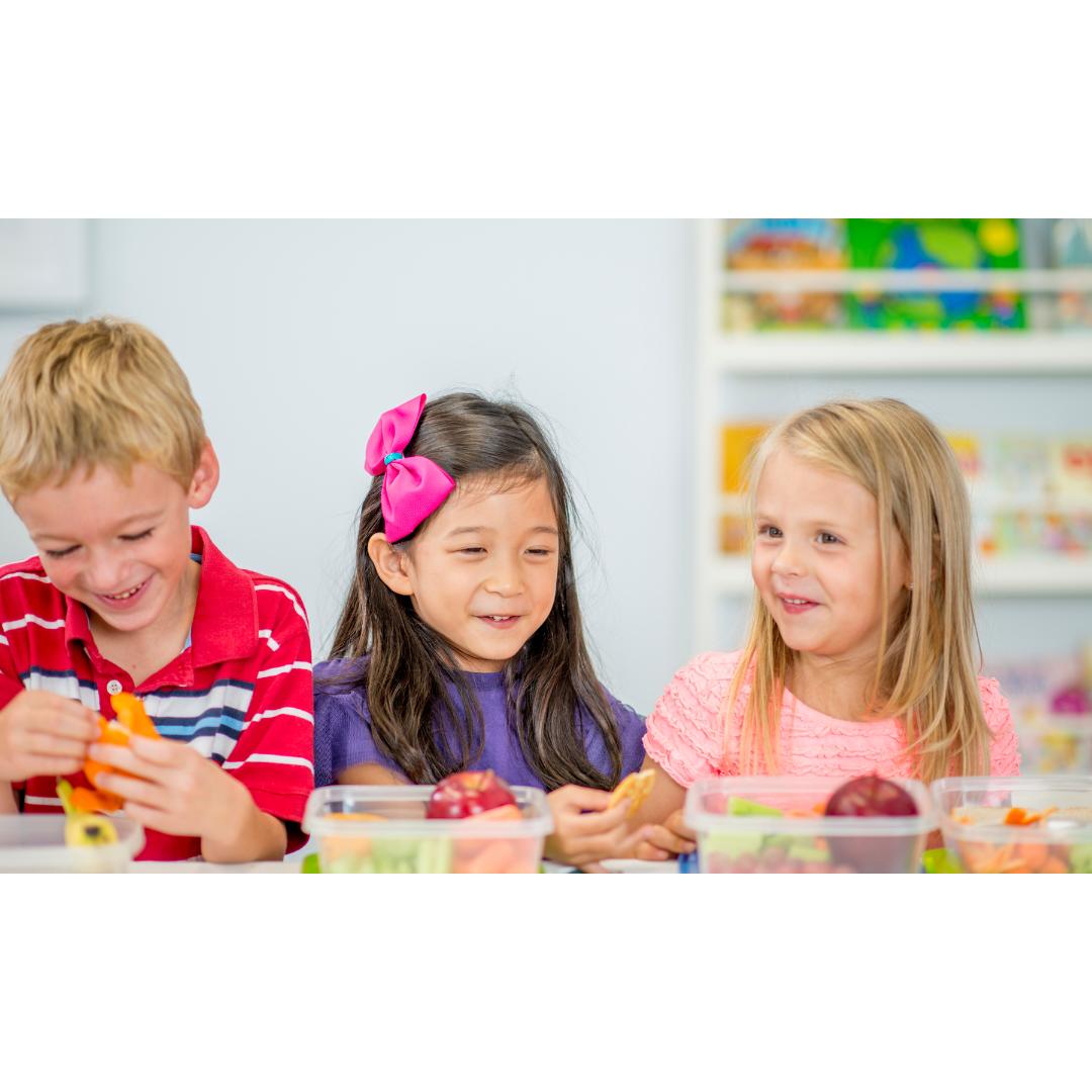 Three children smiling while eating packed lunch