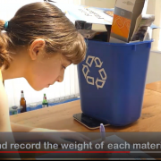 A young girl weighing and recording the weight of cardboard in a blue recycling bin