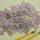 Scrabble letters arranged to spell out Back to School on a sheet of lined paper with two pencils