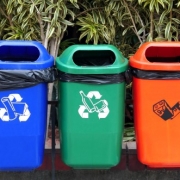 3 brightly coloured Recycling bins in a row hanging on a fence