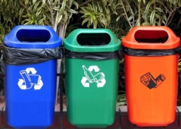 3 brightly coloured Recycling bins in a row hanging on a fence