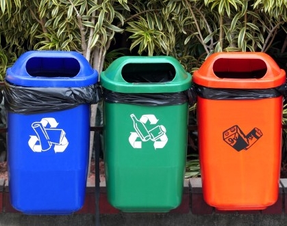 3 brightly coloured Recycling bins in a row hanging on a fence