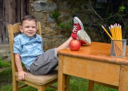 Child sitting outside at desk with legs on desk with apple and pencils