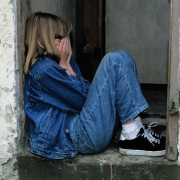 Young girl sitting in a doorway with her hands over her face
