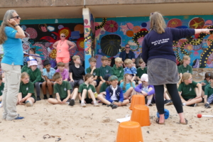 Alex points to the right while an audience of children look right, as they focus on her presentation. While at Exmouth beach