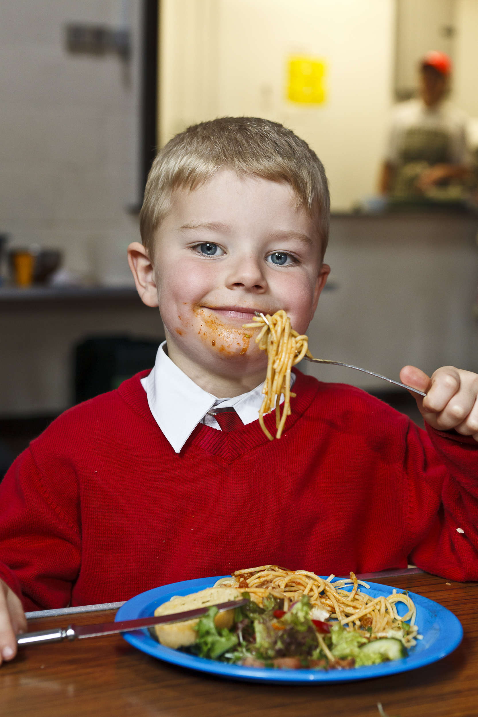 Child smiling and holding a forkful of spaghetti above a plate of spaghetti, salad and bread.