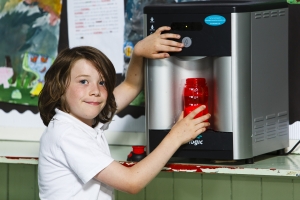 smiling boy in a white polo shirt refilling a reusable plastic water bottle from a water cooler machine