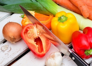 Assorted vegetables including onion, different coloured peppers, garlic, leeks and carrots with a large chopping knife