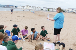 Hannah shows an image to focused children, in the backdrop of Exmouth Beach.