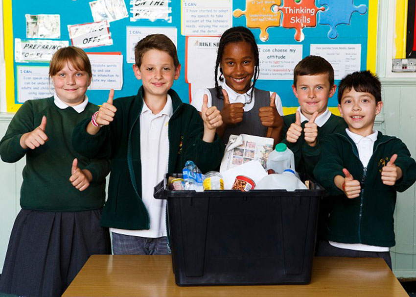 Picture of 5 smiling school children standing behind a recycling box