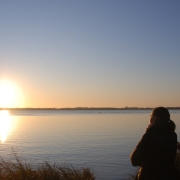 Picture shows a man and child sitting in silhouette watching a winter sunrise over a lake