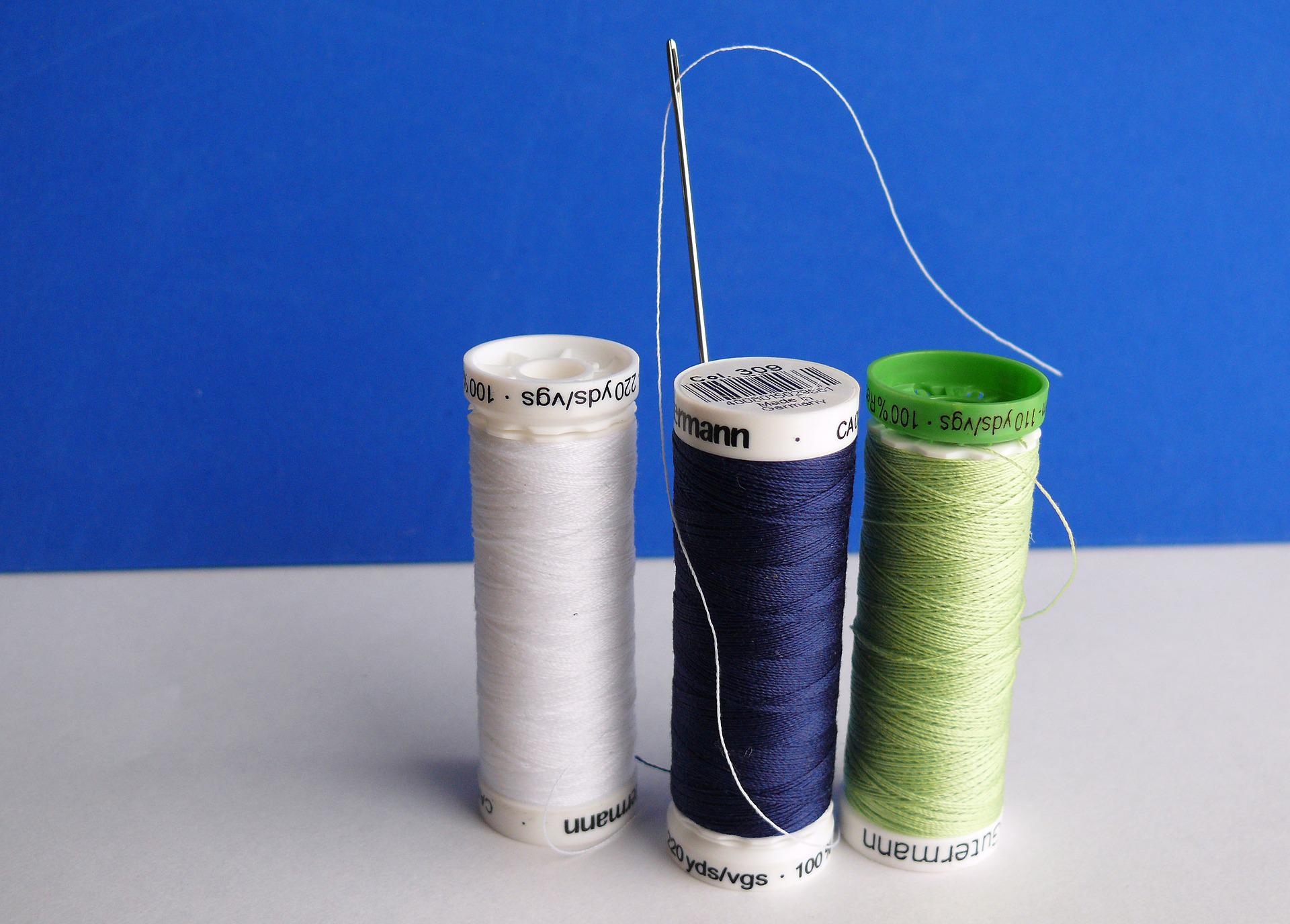 3 spools of cotton thread in navy blue, green and white with a sewing needle