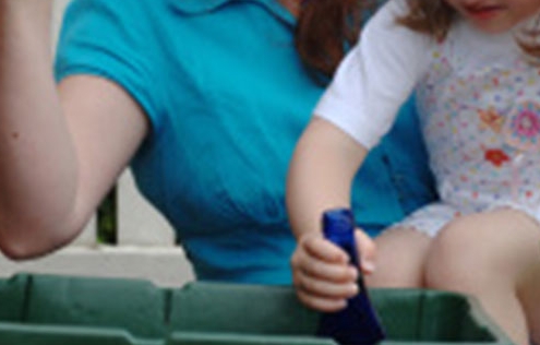 Mother and daughter placing glass bottles in a recycling wheely bin