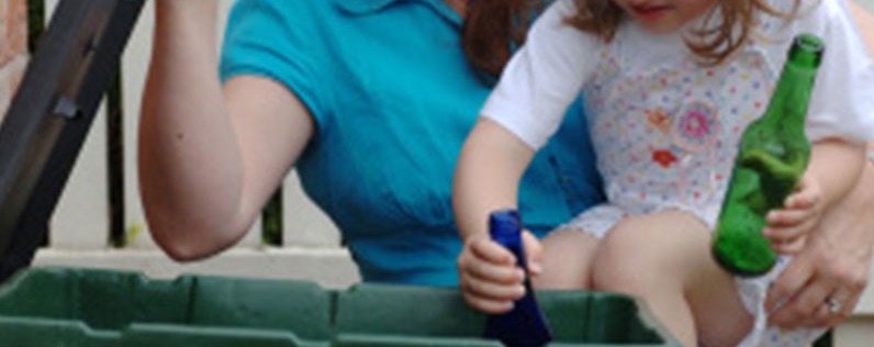 Mother and daughter placing glass bottles in a recycling wheely bin