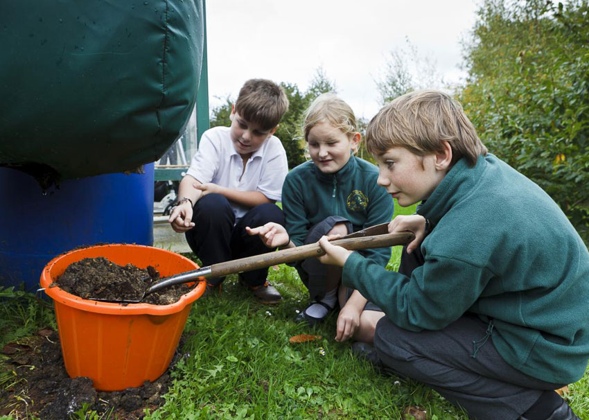 Crouched children around a container of compost beside Ridan composter