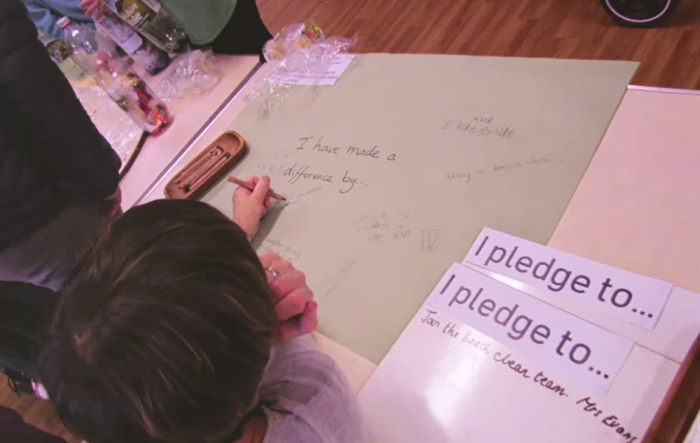 parent writing on a large sheet of paper saying "I have made a difference by..." beside a sign saying I pledge to
