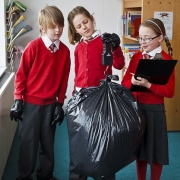 3 children in school uniform using spring balance to weigh a rubbish sack