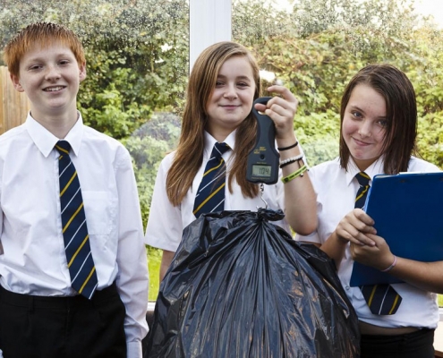 Smiling secondary students with bag of rubbish, scales and clipboard